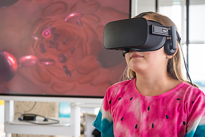 Mädchen stehend mit Virtual Reality Brille auf dem Kopf, vor Bildschirm